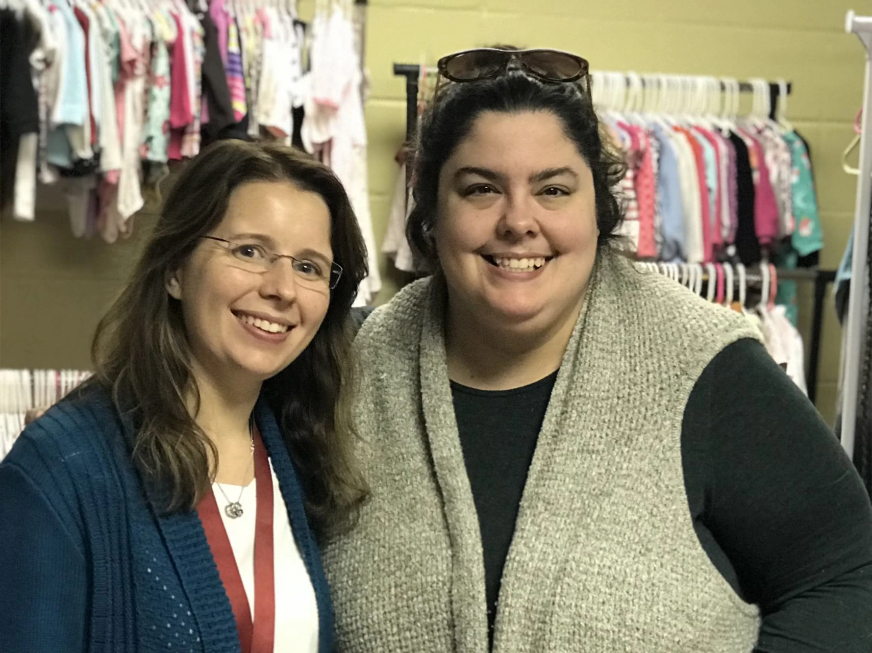 Bethany Comella and Sarah Humphrey standing together in front of a rack of children's clothing